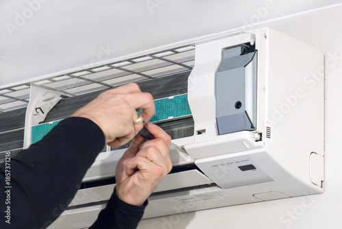Close-up of a technician’s hands using a screwdriver to repair or maintain a wall-mounted split air conditioning unit with the front cover removed