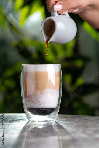 Iced latte in a tall glass, hand-poured, against a green background with a shadow.