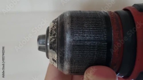 Extreme close up macro shot of hand tightening the keyless chuck jaws of a red cordless power drill to secure the bit