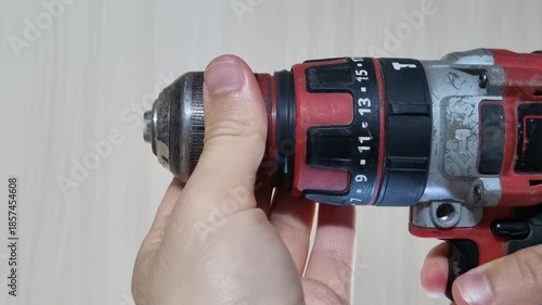 Close up of a hand manually rotating the keyless chuck of a red cordless power drill to close the jaws and secure the drill bit