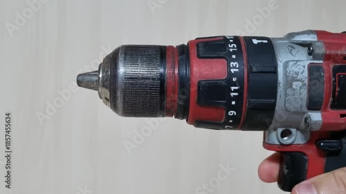 Close up of a hand manually rotating the keyless chuck of a red cordless power drill to open the jaws for removing the drill bit