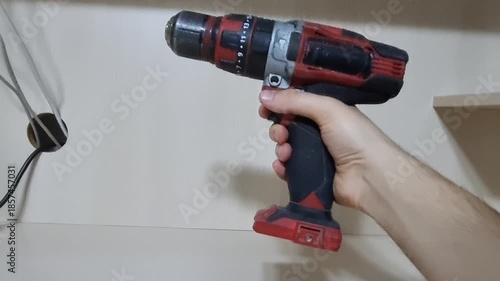Close up side view of a hand pressing release button and removing a rechargeable lithium-ion battery pack from a red cordless power drill