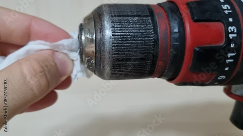 Close up view of a hand cleaning the body of a red cordless power drill with a wet wipe for tool maintenance and hygiene in a workshop