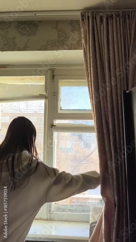 Brunette woman opens blackout curtains in the morning. Blackout curtains on the window. Sleep.