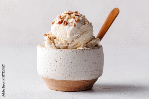 A delicious scoop of vanilla ice cream topped with crunchy nuts is served in a rustic ceramic bowl, with a small wooden spoon.