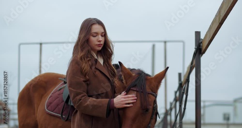 Young woman petting horse on the head near fence