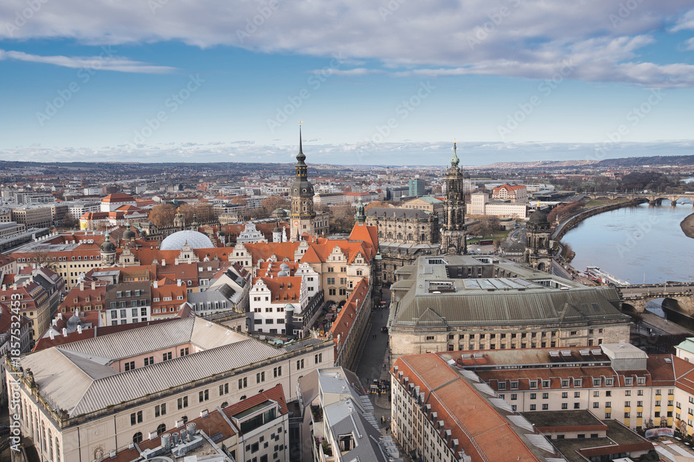 Obraz premium Dresden old town cityscape showcasing historic architecture, including the hofkirche and semperoper, with the elbe river flowing through the urban landscape under a partly cloudy sky