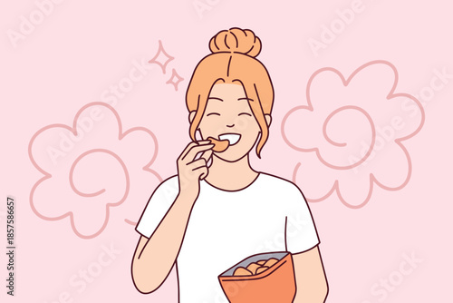 Cheerful girl eats crunchy chips from bag while standing in kitchen or living room. Student or worker taking a break to satisfy hunger with junk food and salty snacks during day.