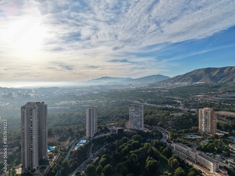 Fototapeta premium bright city scene, sunshine illuminates cityscape alongside mountain range and scattered structures