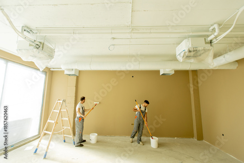 Workers painting an interior wall in a commercial space during daylight hours