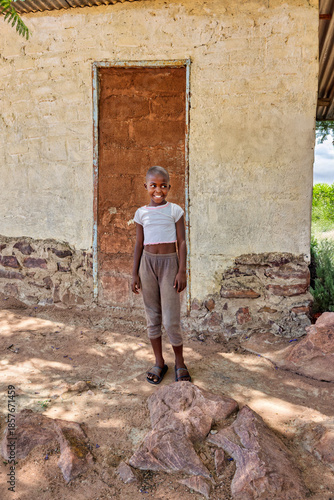 village african single child, outdoors playing in the backyard, standing at home in front of the house wall