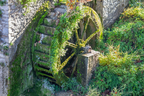 Konstfotografi ​An old, moss-covered wooden waterwheel attached to a stone building, slowly being reclaimed by lush green vegetation and climbing plants