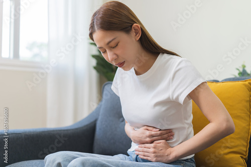 Billede på lærred Sick asian young woman in pain, hand holding belly, stomach pain from food poisoning, girl hurt abdomen ache and digestive problem, gastritis or diarrhea