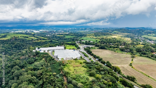 Aerial View of Industrial Warehouse Complex Surrounded by Green Fields and Tropical Forest