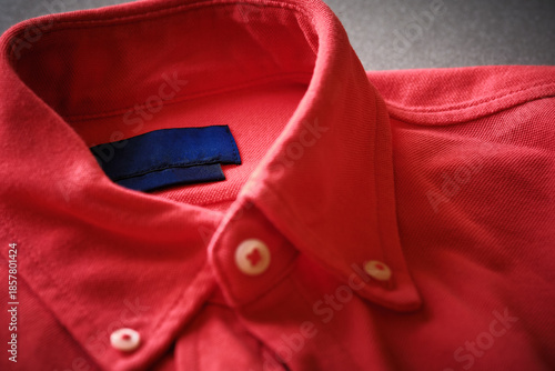 Close-up view of red button-down shirt focusing on collar and buttons. Fabric texture, stitching details of classic casual menswear style