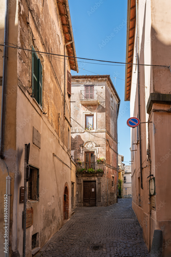 Fototapeta premium Italy - Sutri - Historic center - Narrow cobbled alley with plastered houses, balconies, plants and soft afternoon light