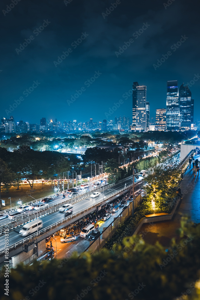 Fototapeta premium illuminated big city skyline at night, cars on road at rush hour, Lumpini park with festive street lights, high-rise skyscrapers and downtown glow at evening, Dusit Central, Bangkok Thailand