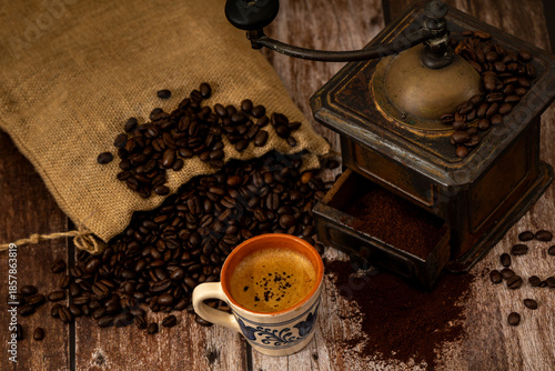A cup of coffee and an old-fashioned grinder on a rustic wood table
