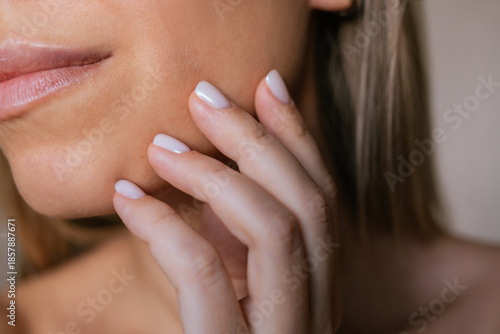 Close-up of young woman touching her cheek with manicured fingers. Natural skin texture, soft light and minimal beauty aesthetic. Skincare, self care and gentle touch concept