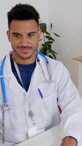 Vertical HD video of young adult Latin American male doctor working on laptop computer at medical consultation. Professional updating medical information digitally. Healthcare business concept
