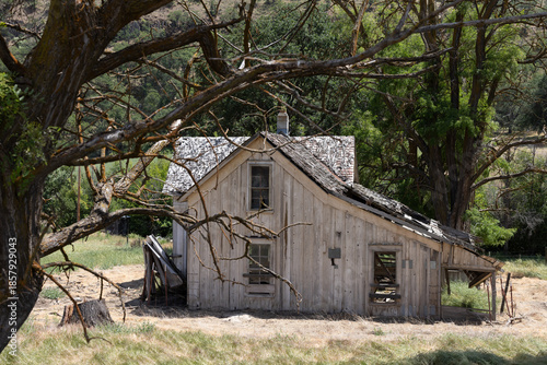 An abandoned home sits among dry grass in a rural farmland area. The house has broken windows and heavy damage.