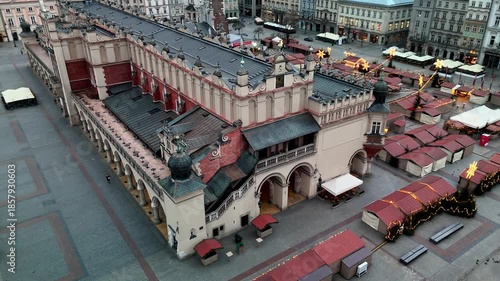 Aerial circling shot of the historic Sukiennice Cloth Hall and the empty, closed Christmas Market stalls covering Krakow's Rynek Główny during a cold winter morning.