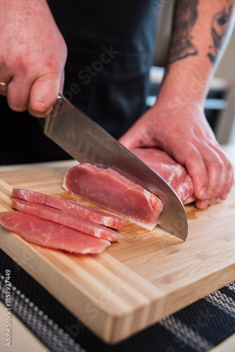 Hands cut a piece of pork with a large knife