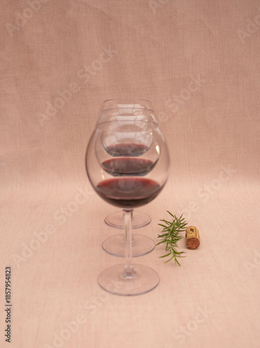 Copas de vino tinto  con tallo largo, en fila; al lado, una ramita de romero y un tapón de botella