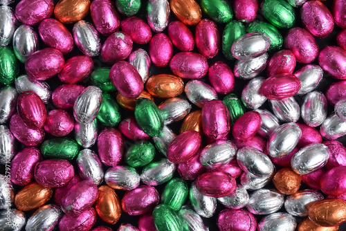 Pink, green, orange, silver and bronze foil wrapped chocolate easter eggs, against a black background.