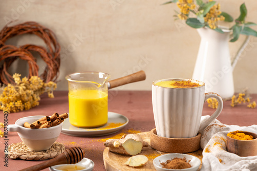 Cozy scene featuring a warm turmeric latte in a ceramic mug alongside fresh ginger root cinnamon sticks and honey. Healthy Golden Milk Turmeric Latte with Ginger and Cinnamon