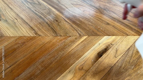 Close up of a hand spraying a cleaning spray bottle with visible mist onto a wooden table. Home cleaning, disinfecting, and household hygiene concept.