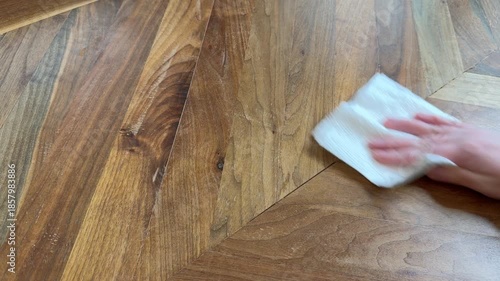 Close up of a hand wiping a wooden table using a paper towel in a circular motion. Everyday home cleaning, surface maintenance, and household hygiene concept.