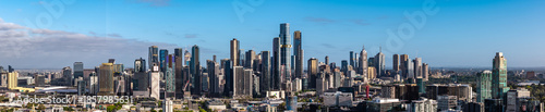 A panoramic view showcasing Melbourne's impressive modern skyline, with numerous towering skyscrapers dominating the urban landscape under a vast blue sky.