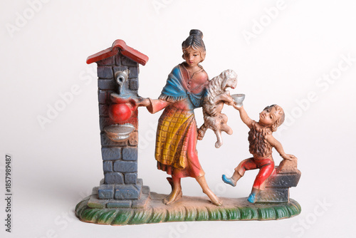 A women pours water from a well for her child and her lamb-figurine