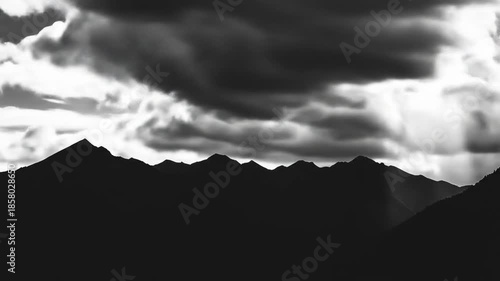Dramatic monochrome mountain range scene with sunlight piercing through clouds