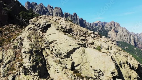 Rugged mountain landscape with dramatic rocky peaks and lush green forest at Col de Bavella, Corsica, under a clear blue sky.