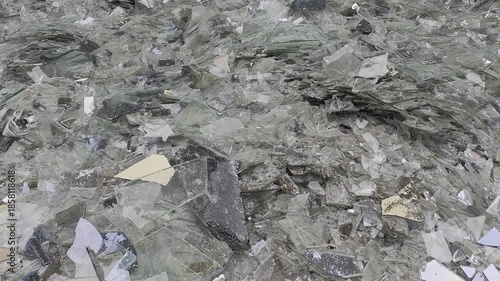 Large pile of broken glass shards scattered in outdoor debris area. Reflective fragments create a chaotic and sharp environment under daylight.