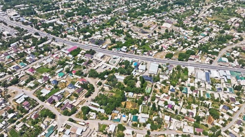 Aerial view captures peaceful suburban town with cars driving on roads. Lush greenery and homes create a serene and natural atmosphere during daytime.