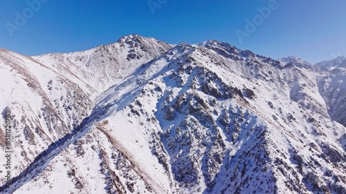 Aerial view captures vast snow-capped mountains in Kyrgyzstan on a sunny winter day. Dolly forward camera movement.