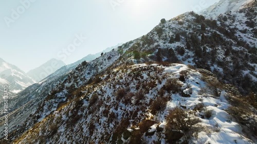 Drone view flying above mountain ridge in Kyrgyzstan at sunny winter day. Dolly forward camera movement.