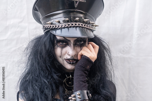 Woman with gothic makeup and piercings wearing black leather cap with spikes looking directly at camera expressing dark power rebellion mystery and intense alternative identity