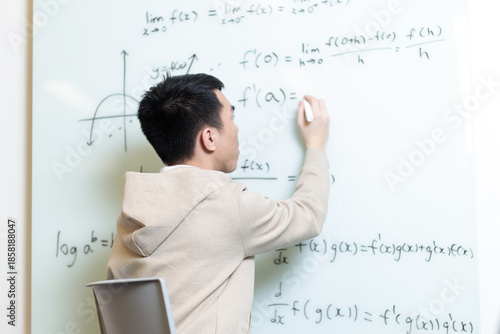 A Chinese student writes complex mathematical formulas on a whiteboard from behind. He works through calculus problems in a modern classroom setting.