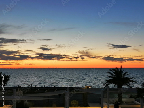 Seashore, silhouettes of people, palm trees, sunset, the sun setting over the horizon