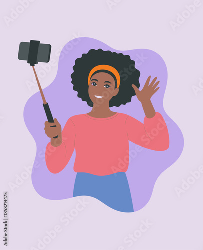 A cheerful young woman poses for a selfie, showcasing her curly hair and vibrant outfit while waving, capturing a moment of happiness and self-confidence in a fun way.