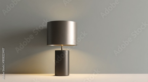 An elegant modern table lamp with a cylindrical fabric shade emits warm glow on a neutral backdrop,