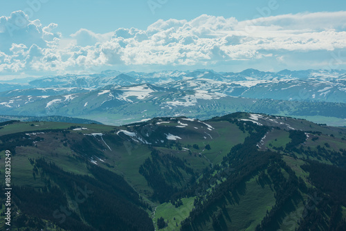 Foto Aerial sunlit top view above forest hills and big snowy mountain range under lush clouds in changeable weather