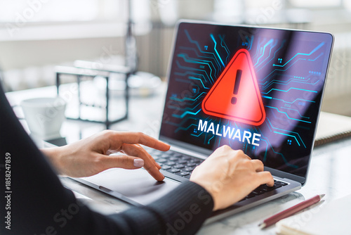 Woman using laptop with malware alert warning on screen at modern office desk showing cyber threat concept and digital data security breach. © Who is Danny