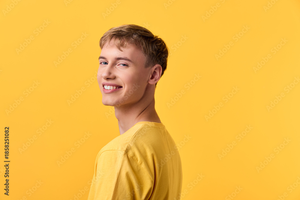 Obraz premium Man smiling in a yellow shirt against a yellow studio background, posed naturally for fashion and lifestyle stock, capturing bright mood, casual style and confident expression.