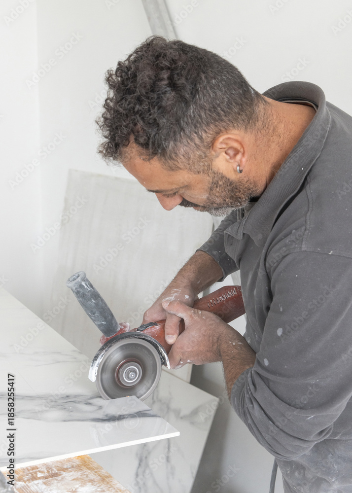 Obraz premium Craftman in grey shirt cuts a gray marble tile using an angle grinder. Handy men at work, hands closeup