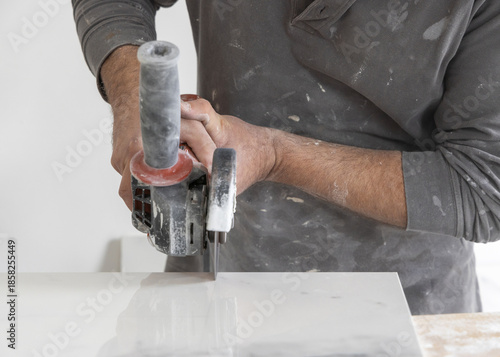 Craftman in grey shirt cuts a gray marble tile using an angle grinder. Handy men at work, hands closeup